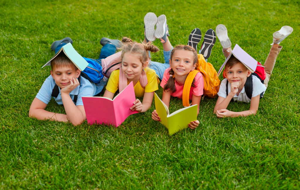 Quatre enfants qui travaillent couchés sur l'herbe