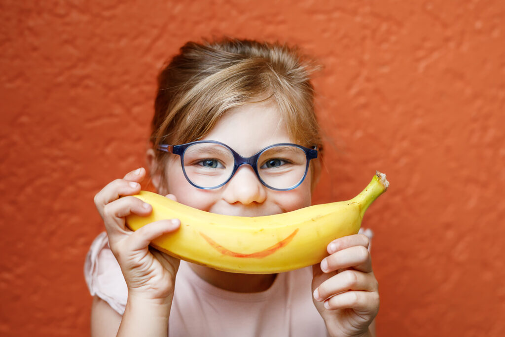 Petite fille qui sourit avec une banane devant la bouche