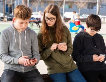 Groupe de trois élèves regardant leur téléphone dans un parc