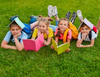 Quatre enfants qui travaillent couchés sur l'herbe